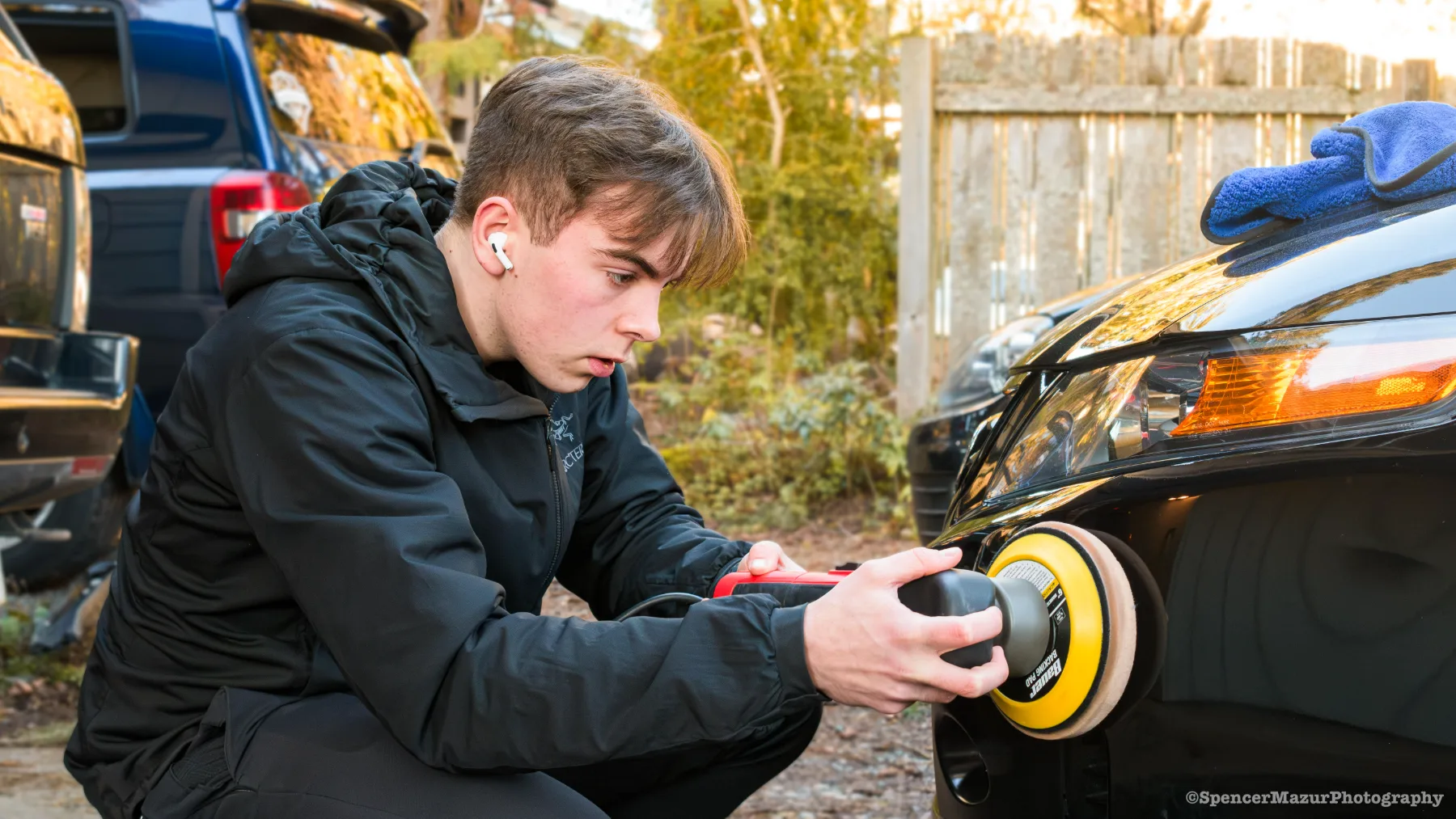 Frank machine-polishing the front bumper of a black car next to its headlight